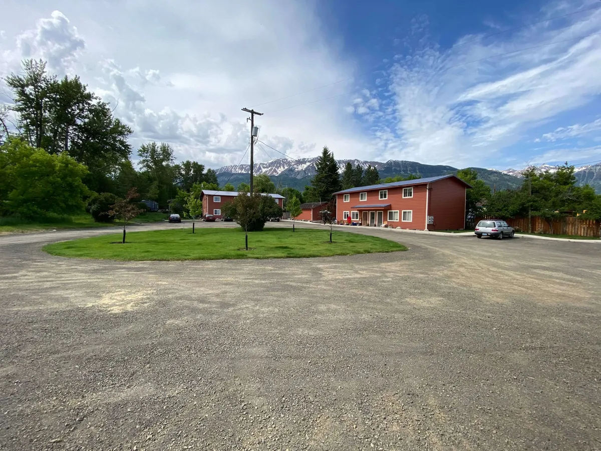 This image features a striking red building set against a majestic mountain backdrop, with a lush green grass circle in the foreground. The inviting outdoor scene is ideal for family gatherings, casual strolls, and picnics. Seasonal blooms and natural beauty add to the sense of adventure and relaxation.