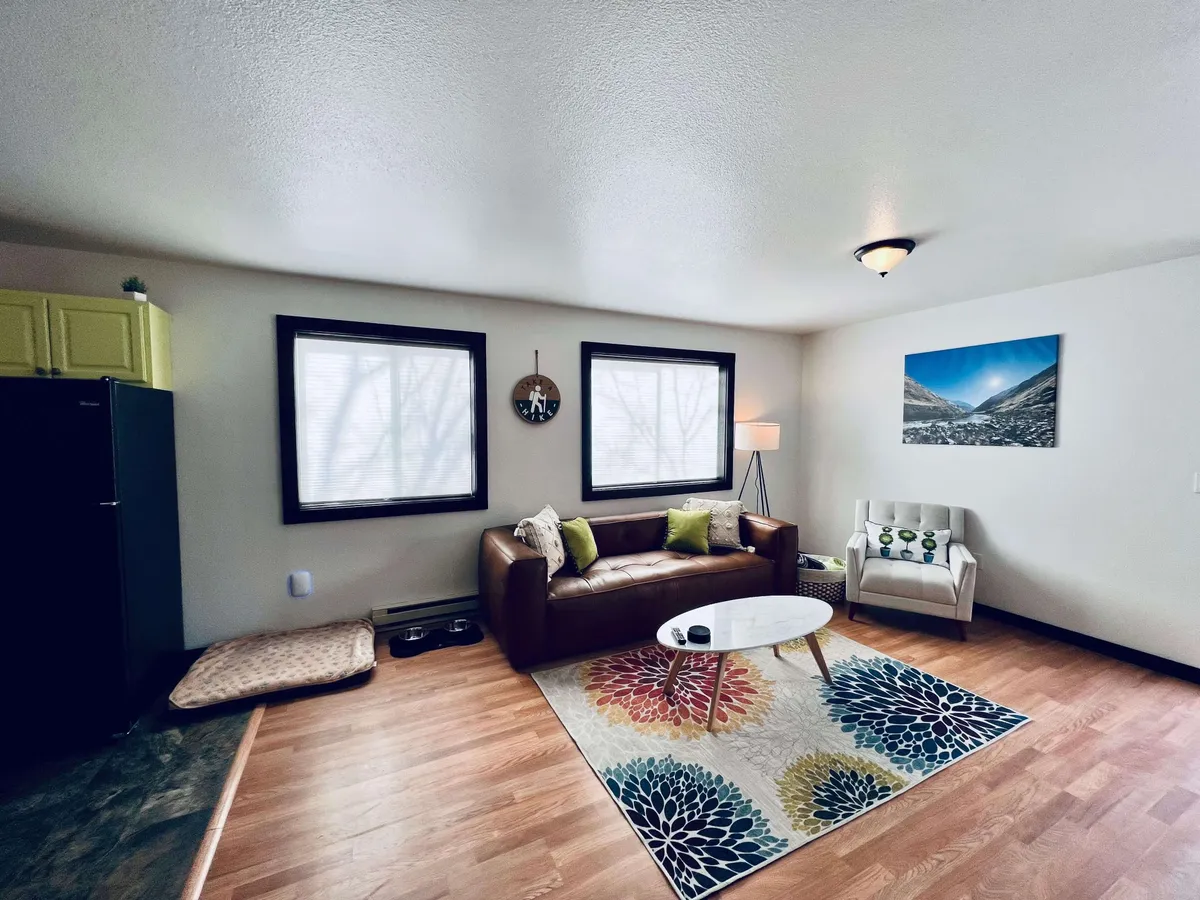A cozy and modern living room featuring a leather sofa set atop a colorful area rug, decorative wall art, and a warm lamp. The space is arranged for both relaxation and socializing, inviting guests to read, entertain, or enjoy intimate conversations.